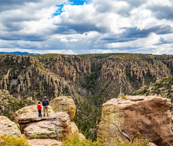 Hikers overlook Chiricahua National Monument in Arizona on a partly cloudy day.