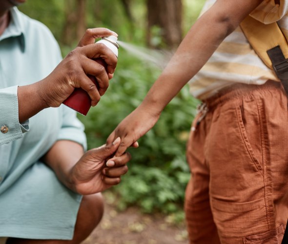A parent helps their child apply bug spray to prevent ticks before a hike.