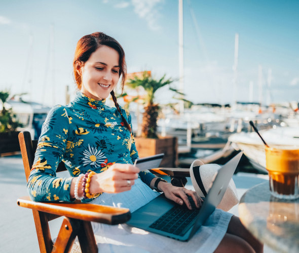 A woman sits outside on a dock with her computer and a coffee.