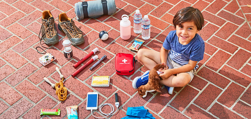 boy seated on ground with an array of emergency road kit essentials