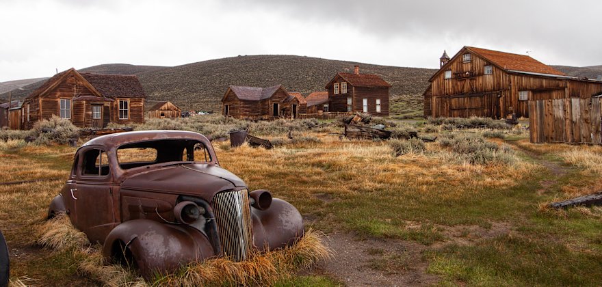 Rusted car and abandoned buildings in the ghost town of Bodie, California.
