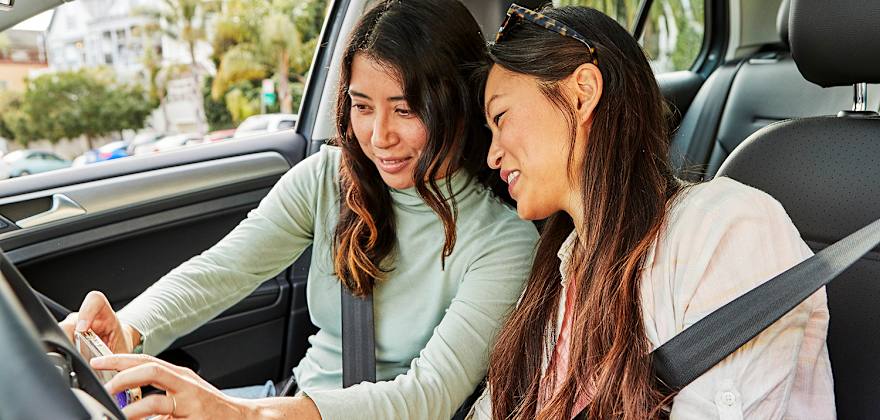 two women in parked car looking at mobile device
