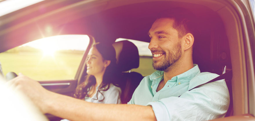  A man and woman smiling while they drive in a car with the sun shining over the horizon