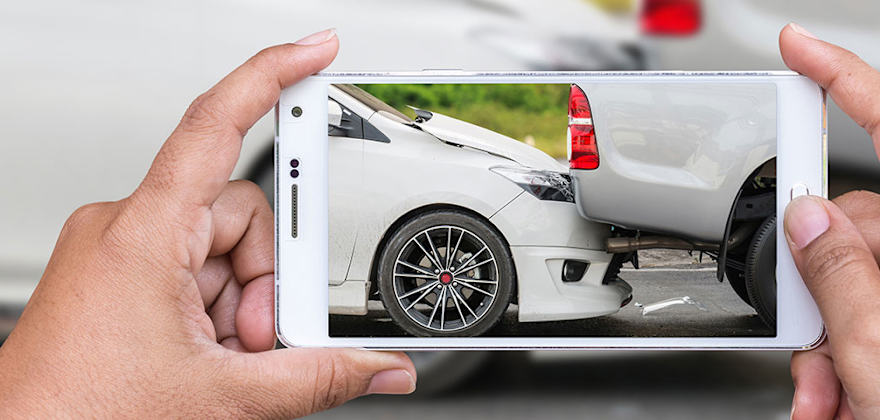 A person's hands on their mobile phone taking a picture of their recent collision for insurance