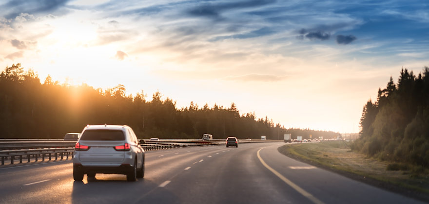 The back of a car as it drives on a three lane freeway as the sunsets