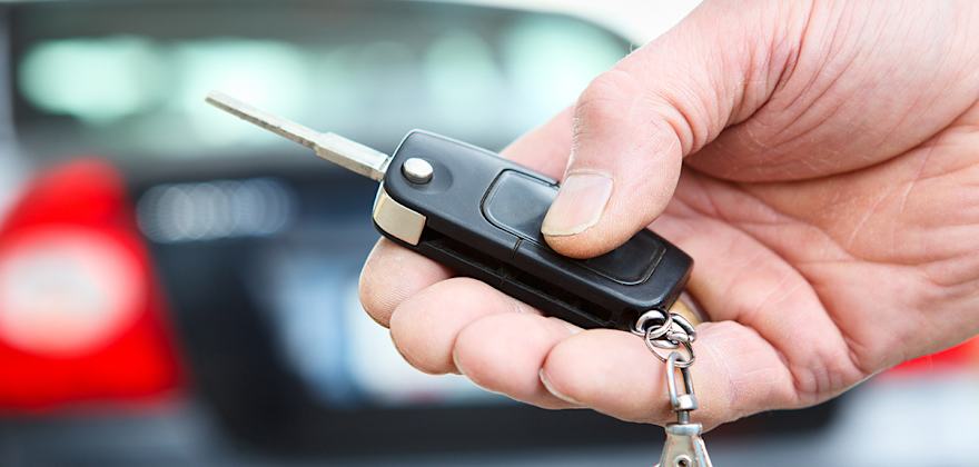 A person's hand holding a rental car key with a blurred view of the car behind