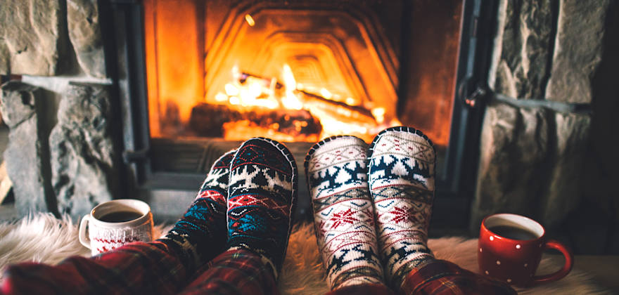 A couple warm their feet in front of a fire.