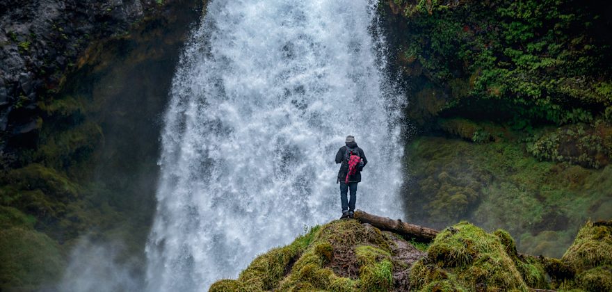 hiker takes in view of Sahalie Falls from moss-covered rock, near Sisters, Oregon