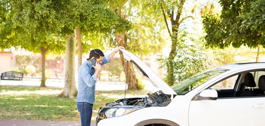 A man looks under the hood of his small white SUV.