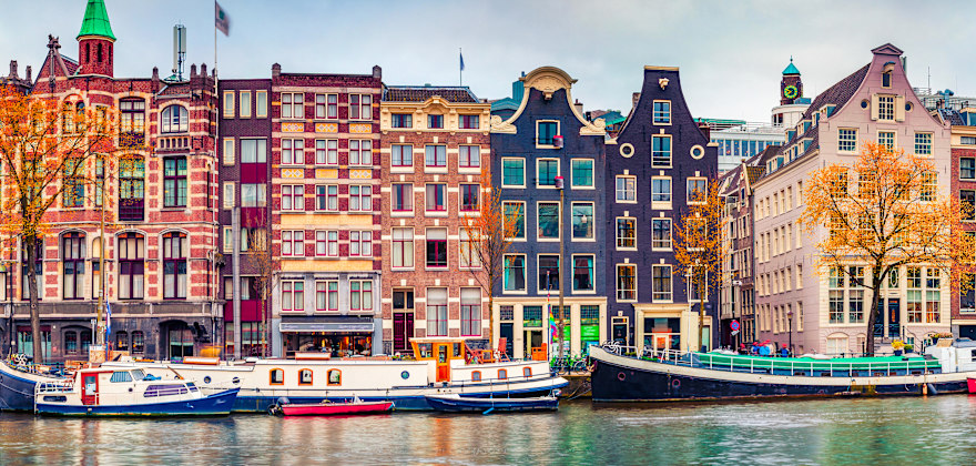 Panoramic autumn view of Amsterdam's colorful row houses along a canal.