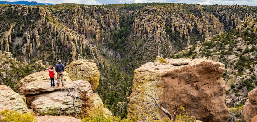 Hikers overlook Chiricahua National Monument in Arizona on a partly cloudy day.