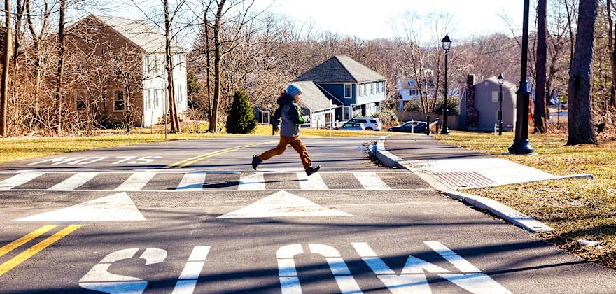 A child runs across a crosswalk on a fall day.