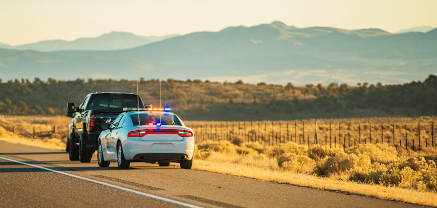 A Utah Highway Patrol car with flashing lights is pulled over behind a black truck on the side of a highway.