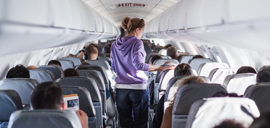 A woman in a purple sweatshirt walks up the aisle of a full airplane.