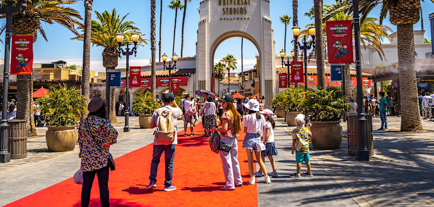people walk towards Universal Studios Hollywood on a red carpet surrounded by palm trees