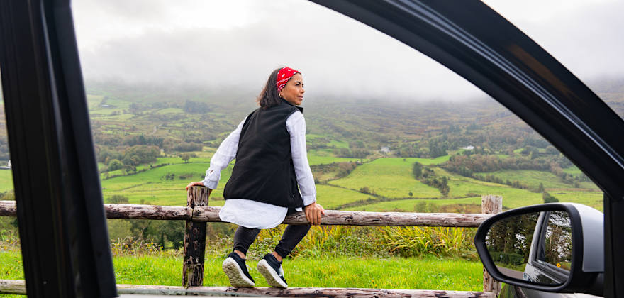 A woman sits on a fence beside her rental car in Spain.