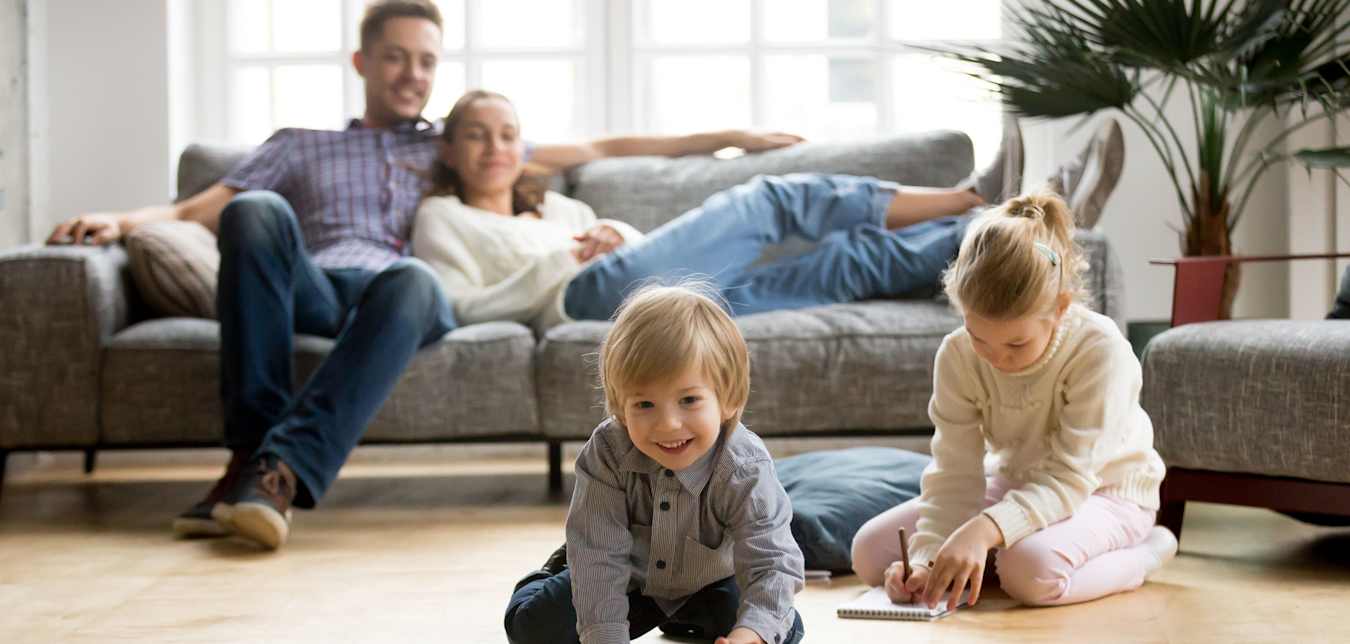 Little boy reaching for a toy car on the floor while his parents and sister watch