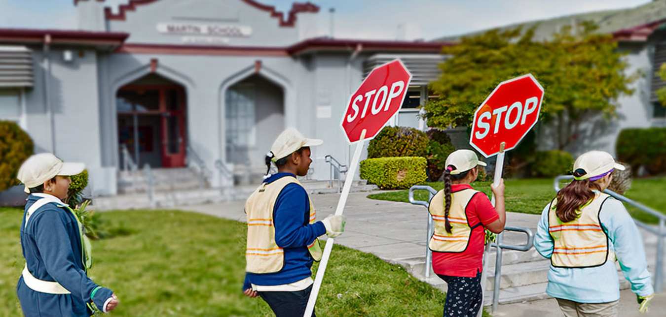  AAA School Safety Patrol students walking in a line in front of their school holding stop signs.