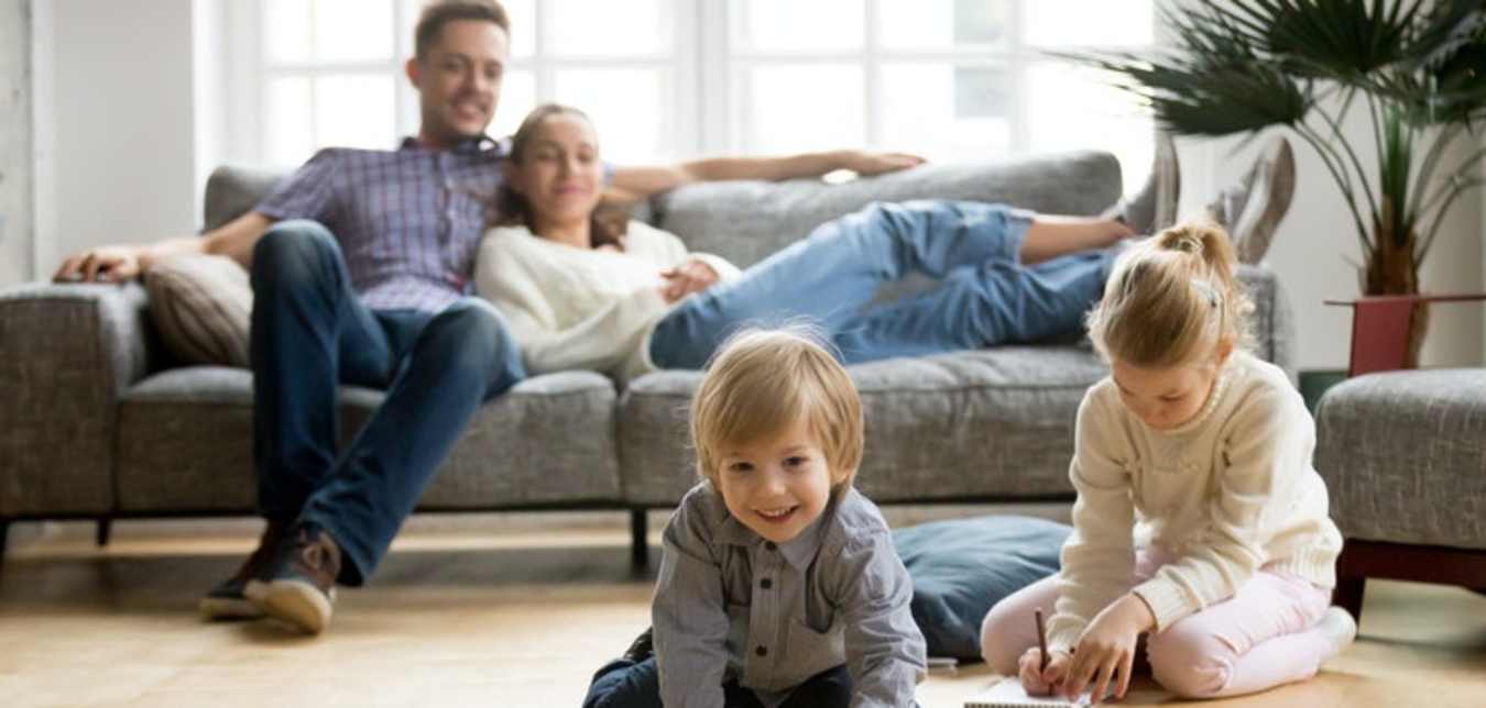 parents relax on the couch while they watch their children play on the floor
