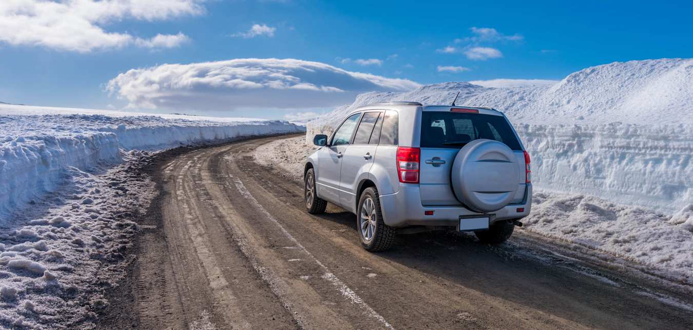 A small SUV drives on a plowed road in Iceland.