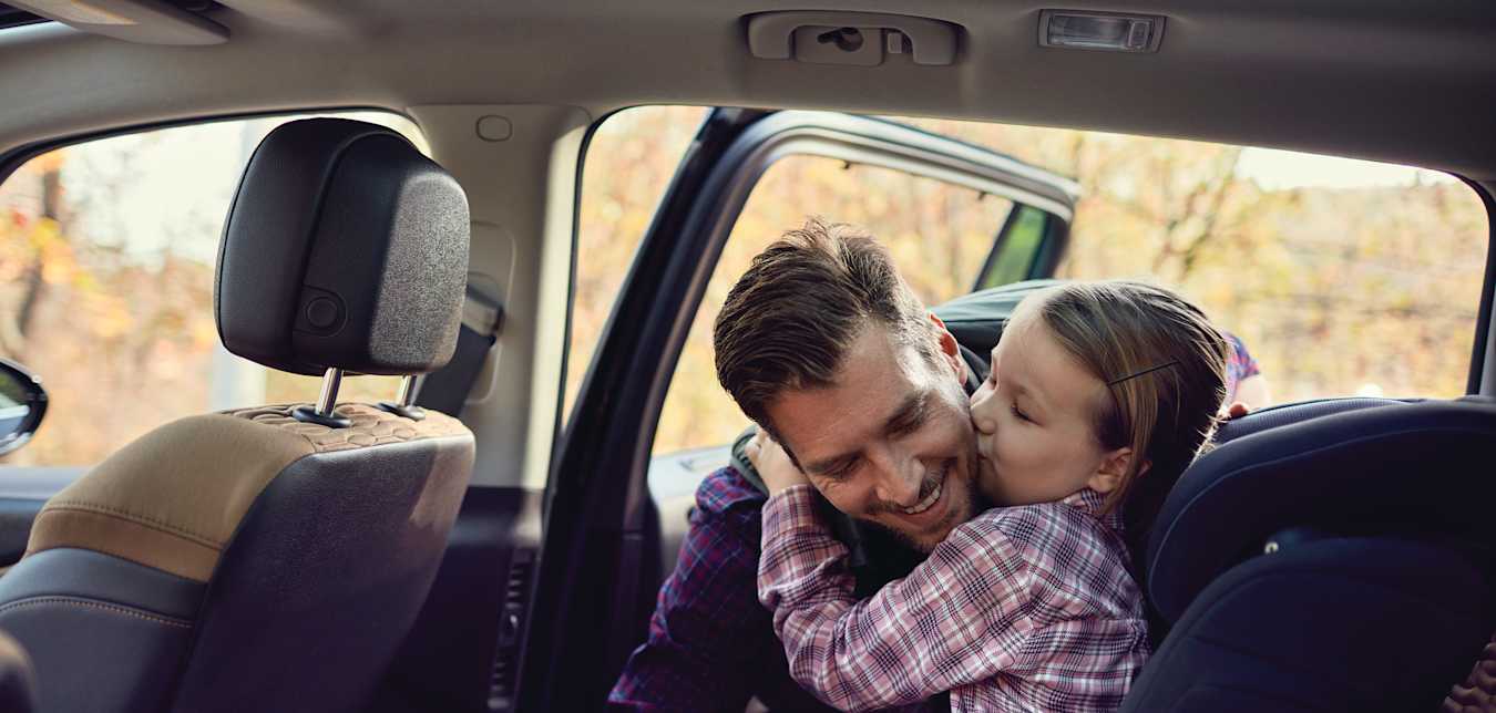 Father buckling his daughter into her car seat in an automobile covered by AAA insurance.