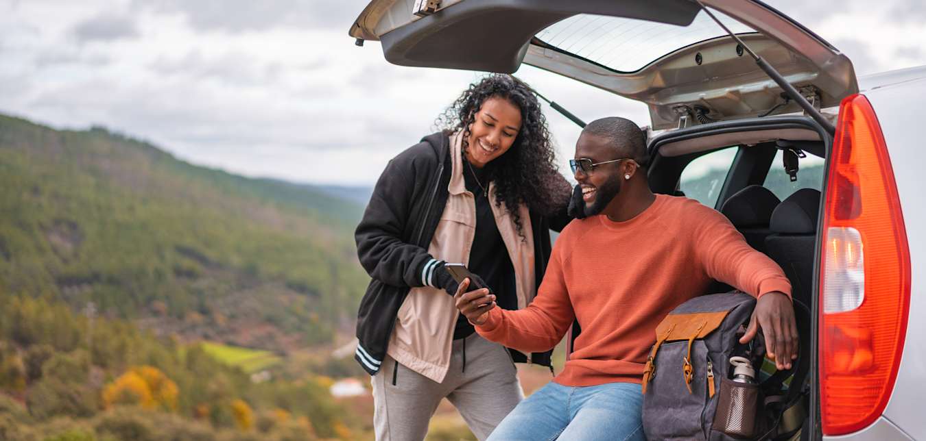 AAA Members look at their phone by their car at a scenic vista