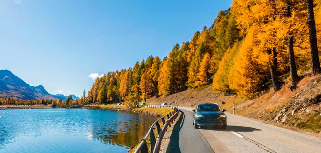 car driving on the road alongside a lake during the fall