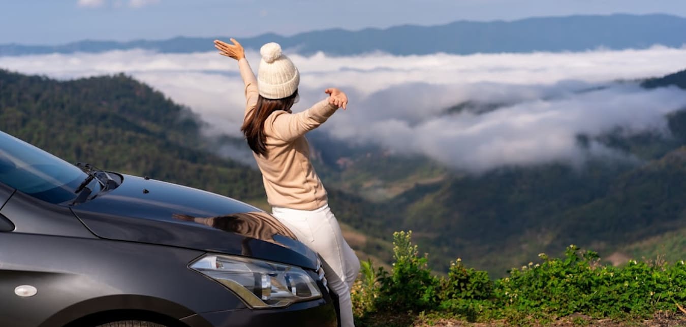 women wearing a beaning sitting on the hood of a car looking out to a valley