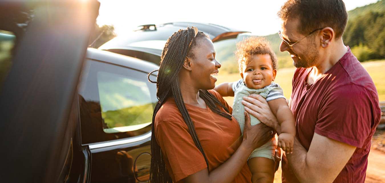 interracial couple with their baby standing outside their Hertz car rental