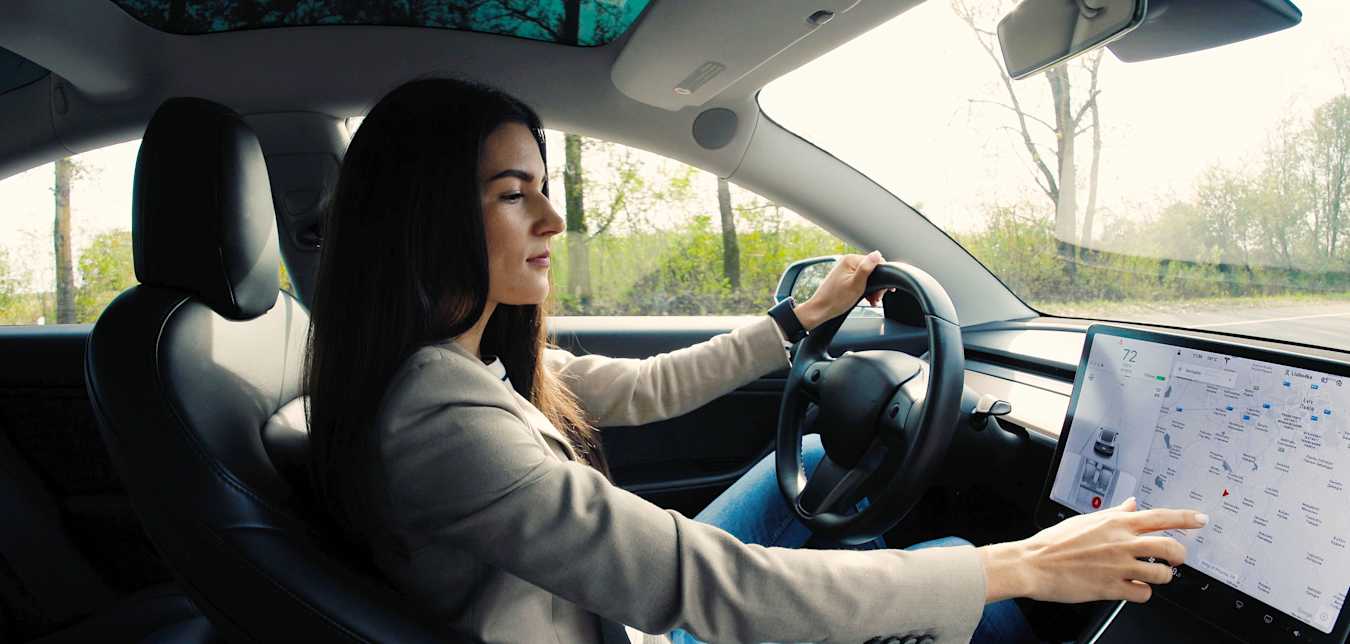 A woman uses a large dashboard infotainment touch screen while driving.