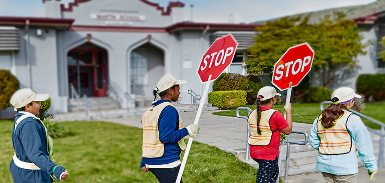  AAA School Safety Patrol students walking in a line in front of their school holding stop signs.