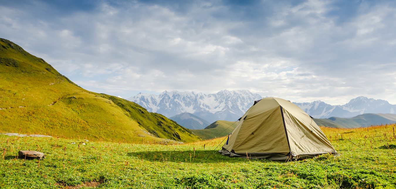 Pitched tent on the grass overlooking beautiful view.