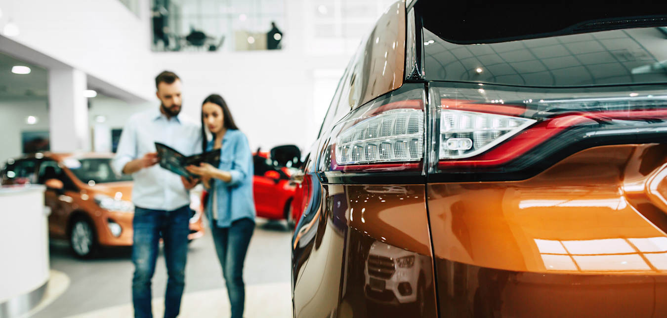 A couple shop for a car in a car dealership.