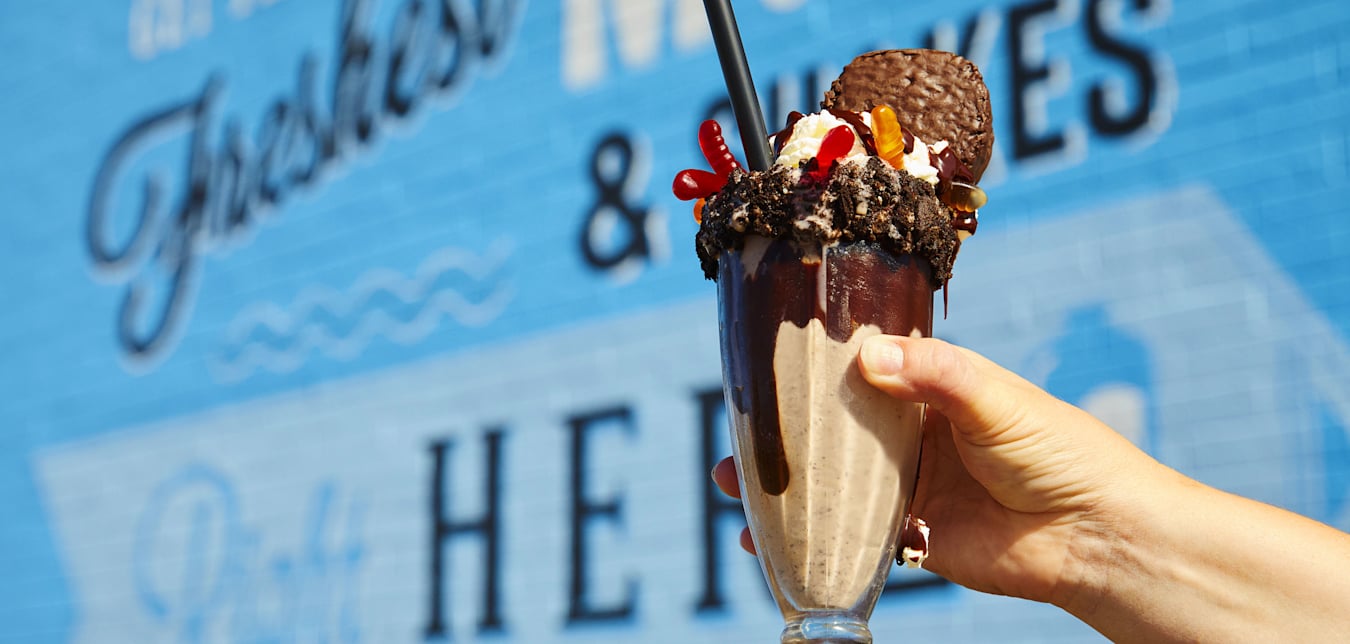 A glass of the The Dirt Stack milkshake, which is a vanilla shake in a chocolate syurp lined glass, topped with oreo crumble, gummy worms and a hostess cupcake, from Danzeisen Dairy Creamery Store.