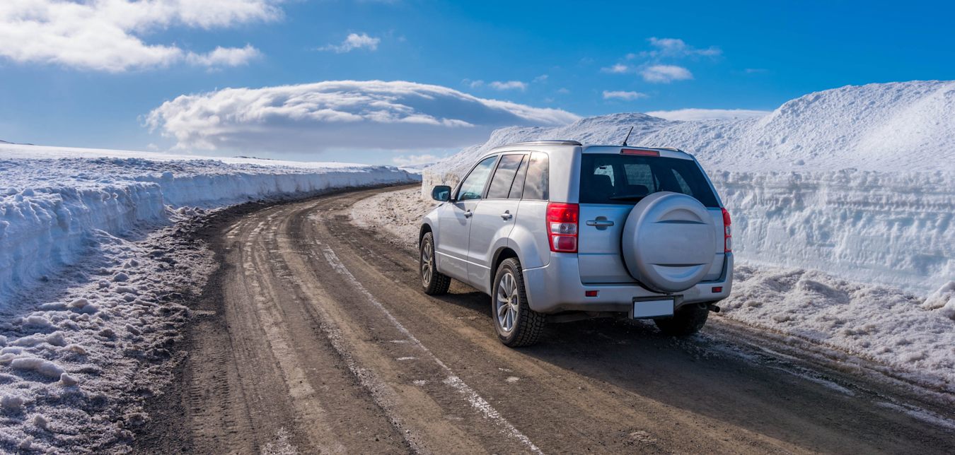 A small SUV drives on a plowed road in Iceland.