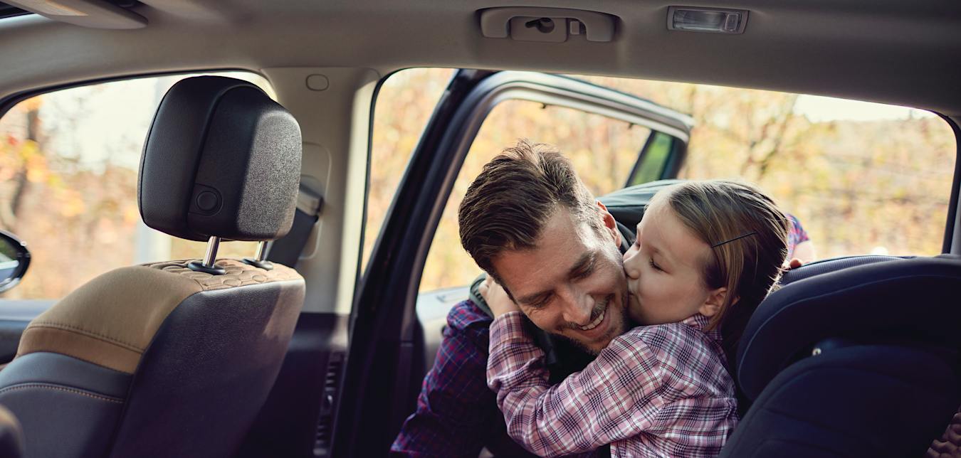Father buckling his daughter into her car seat in an automobile covered by AAA insurance.