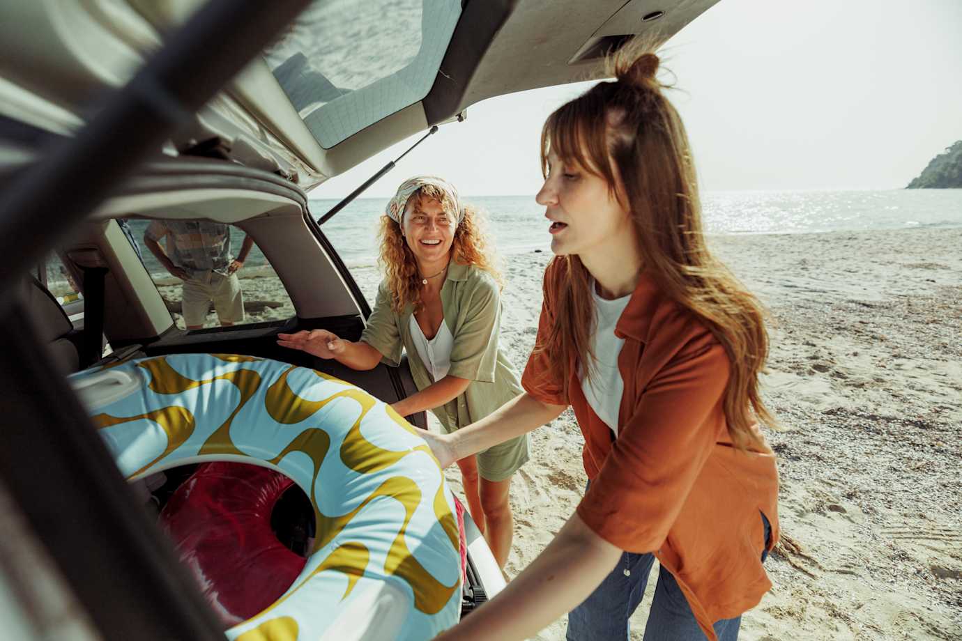 Women putting inflatable tube in back of car at beach