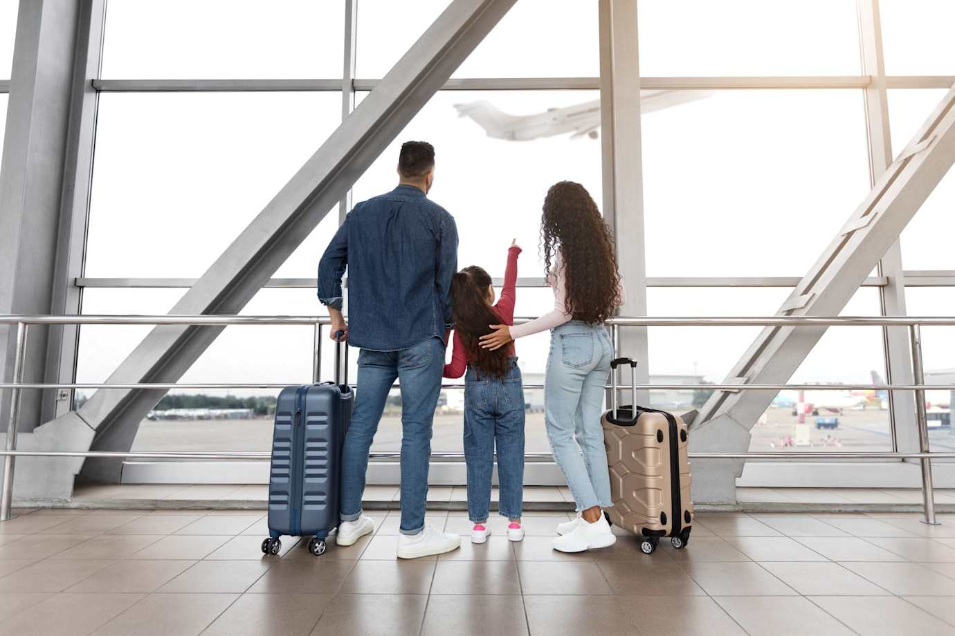 family with luggage watching plane take off from airport window