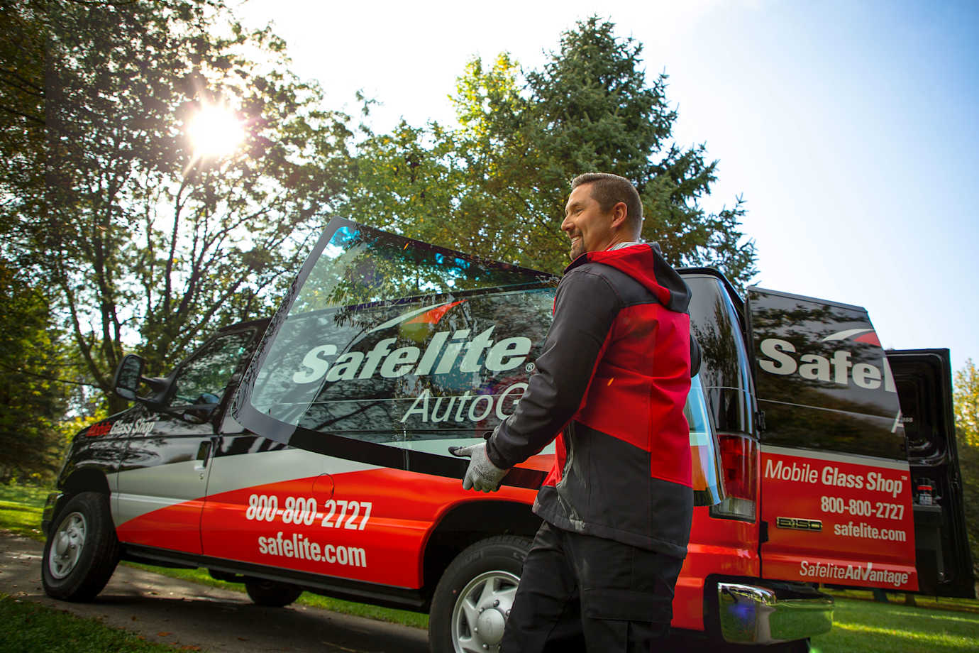 Safelite AutoGlass technician holding a windshield replacement next to his van