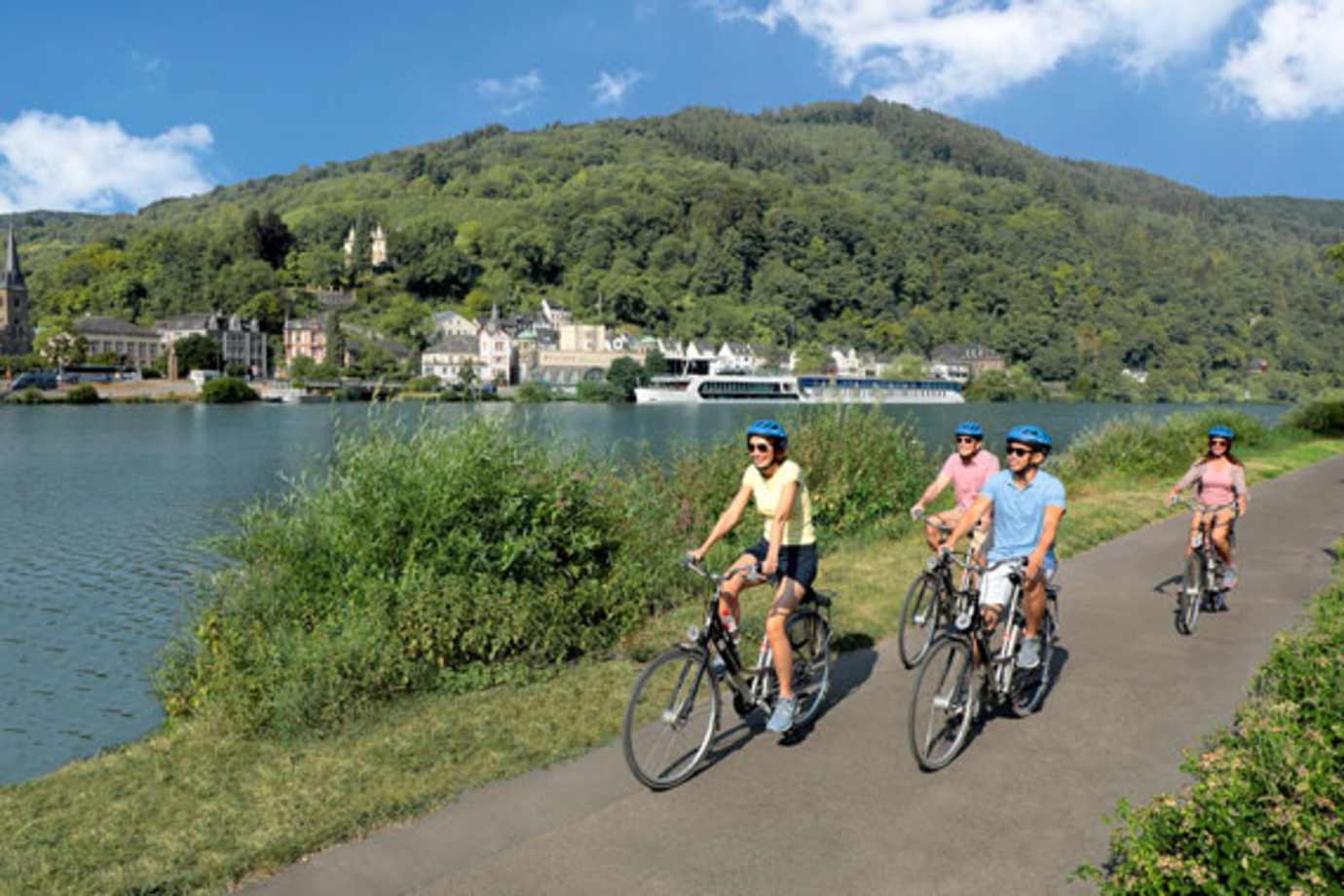 people riding bikes next to a river with an amawaterways ship in the background