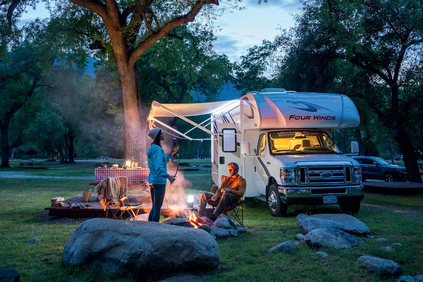 A couple relax around a campfire outside their RV