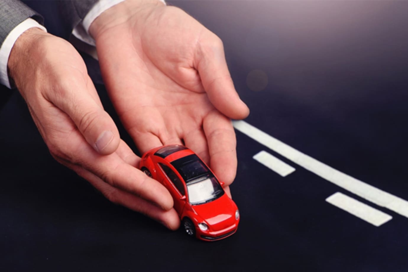 Hands representing a AAA auto insurance agent gently placing a car on the road