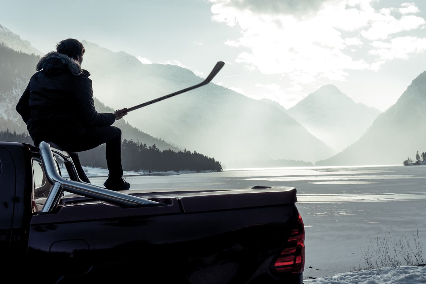 Man sitting in back of pickup truck looking at mountains