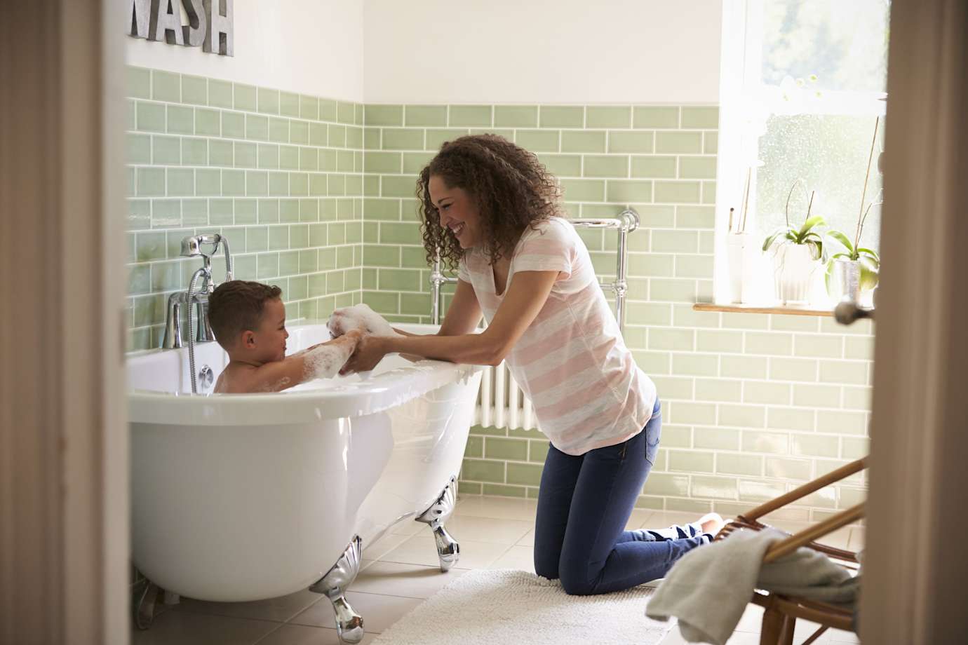A mom bathes her son in a clawfoot bathtub.