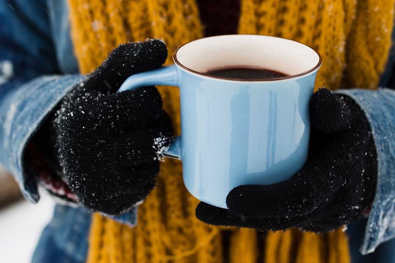 A person holds a blue coffee mug on a snowy morning.