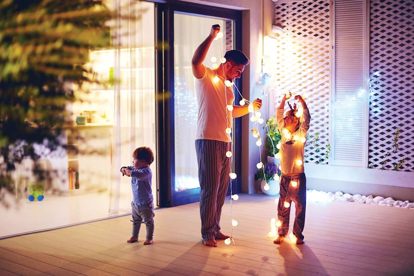 A dad and his two children hang up led string lights on their patio.