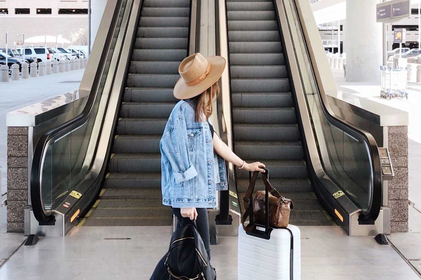 A woman walks through the airport with her white rolling luggage.
