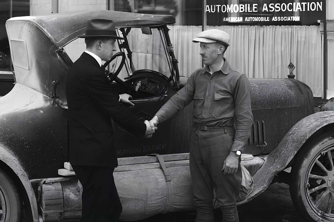 Two men shake hands in a historic black and white photo outside of a AAA office.
