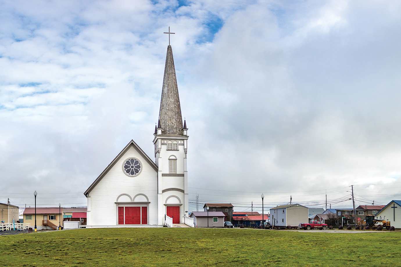 A white church in Nome, Alaska with green grass and a blue sky.