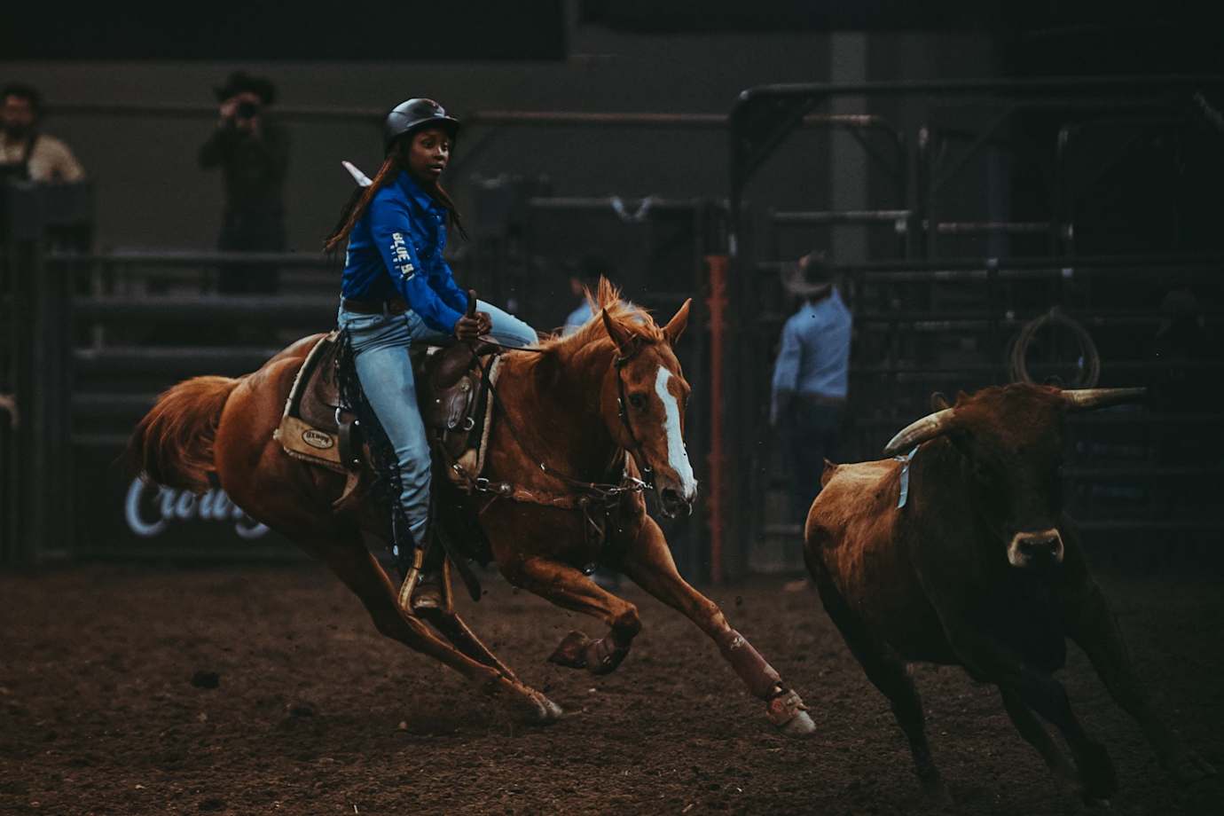 A female rodeo rider on horseback, roping cattle in the arena